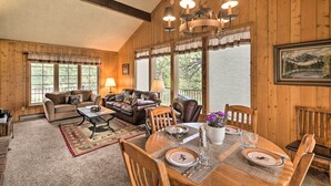 A cozy living room with a fireplace, wooden walls, and a dining area with a table set for four. - 'rocky Mountain Breezes' Cabin: Grill + Deck! (Estes Park)