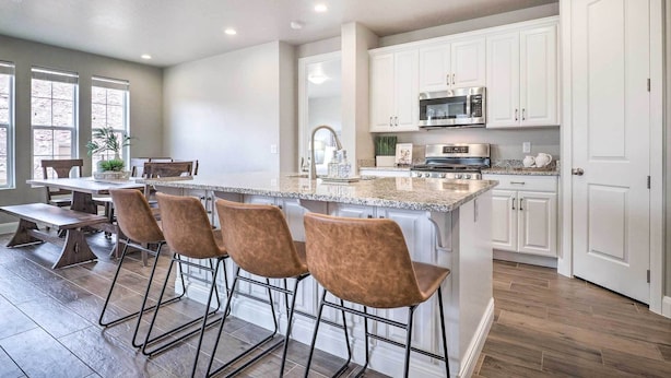 A modern kitchen with white cabinets, a central island with bar stools, stainless steel appliances, and a large window providing natural light. - Lazy River, Arcade & Pickleball in Washington! (Washington)