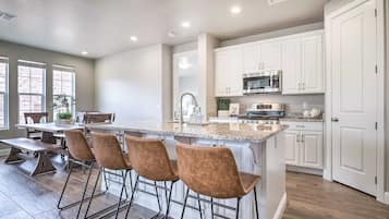 A modern kitchen with white cabinets, a central island with bar stools, stainless steel appliances, and a large window providing natural light.