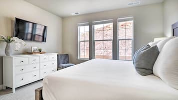 A bedroom with a large bed, a dresser, a TV, and a window with a view of a rocky landscape.