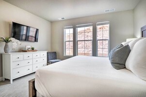 A bedroom with a large bed, a dresser, a TV, and a window with a view of a rocky landscape.
