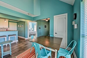 A dining area with a wooden table and turquoise chairs, a kitchen with white cabinets, and a teal-colored wall.