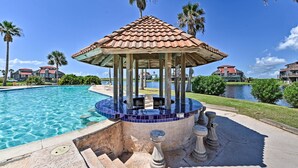 A gazebo with a tiled roof, a pool, and palm trees.