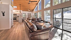 A spacious living area with a large leather sofa, a dining table, and a view of a snowy landscape through large windows. - Mtn-view Cabin w/ Game Room & Deck in Flagstaff (Flagstaff)