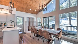 A modern kitchen with a central island, wooden ceiling, and large windows offering views of a snowy landscape. - Mtn-view Cabin w/ Game Room & Deck in Flagstaff (Flagstaff)