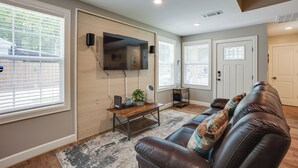 A living room with a leather couch, a wooden coffee table, and a flat-screen TV mounted on the wall. - Lake Conroe Vacation Rental 1/2 Mi to Boat Launch! (Willis)