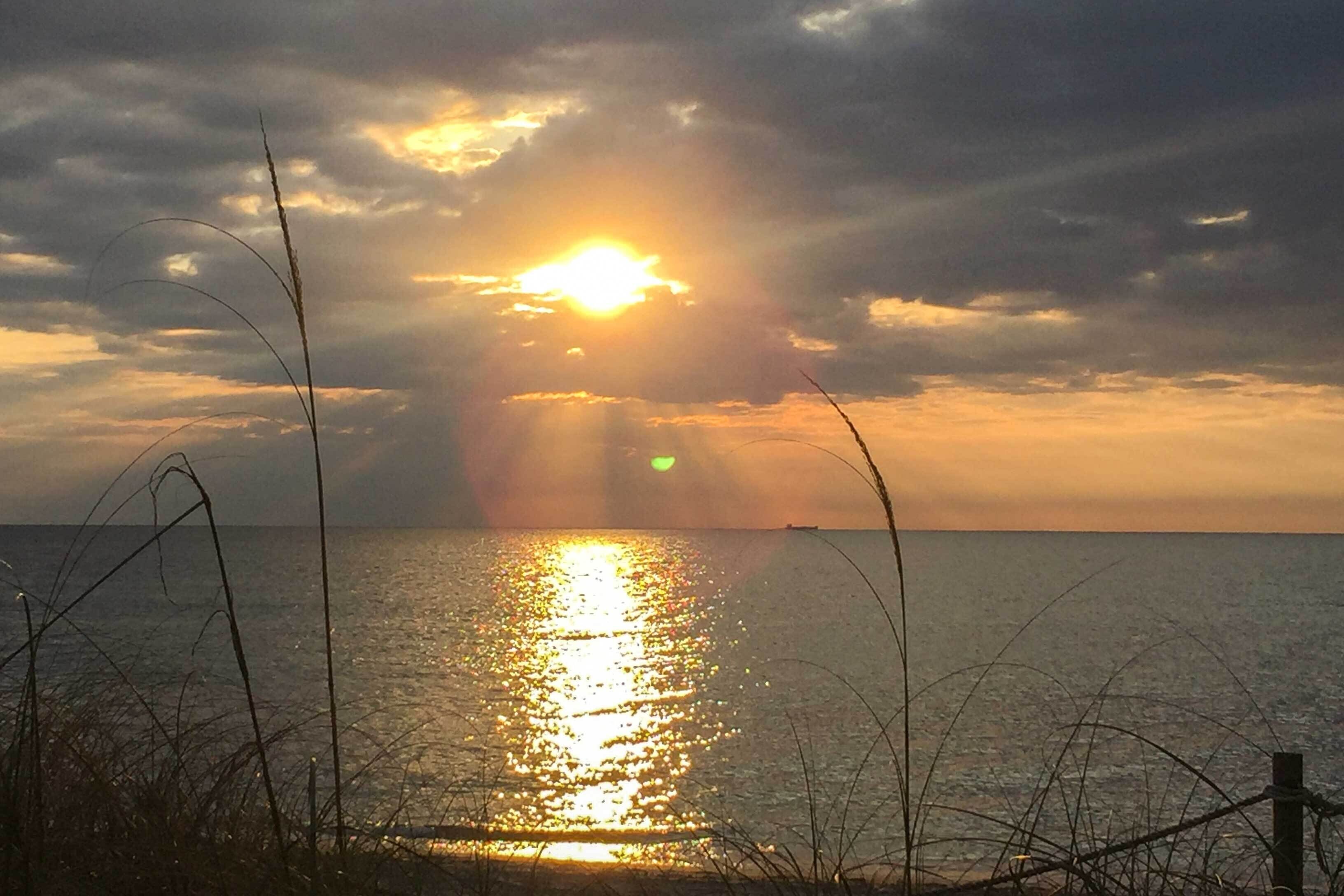 Un coucher de soleil sur une étendue d’eau, avec une clôture au premier plan.