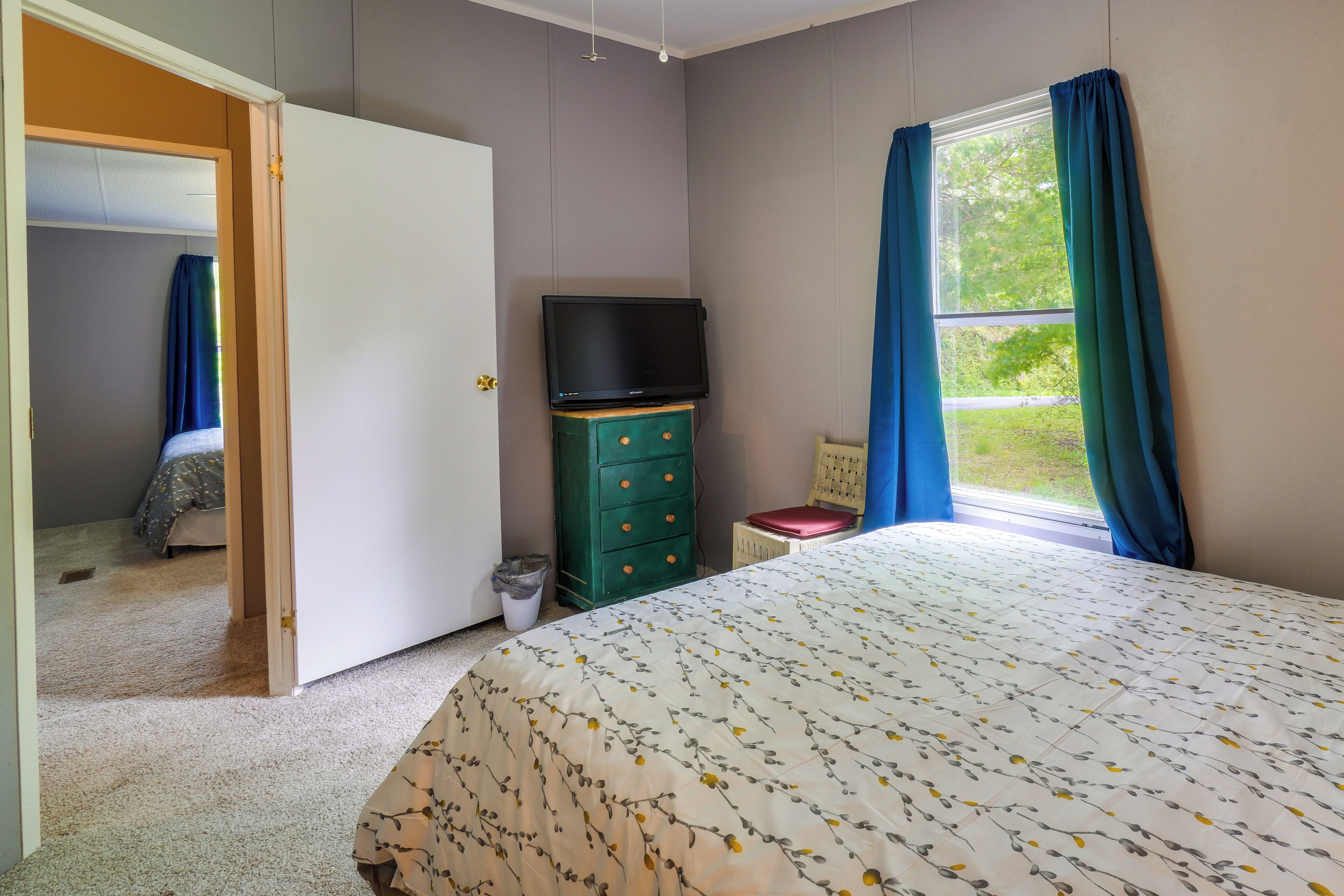A bedroom with a bed, a dresser, a television, and a window with curtains.