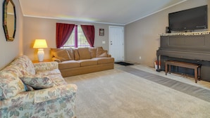 Ein Wohnzimmer mit einer Couch, einem floralen Sessel, einer Lampe, einem Fernseher und einem Klavier.
