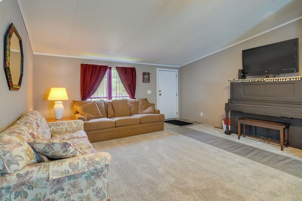 A living room with a sofa, a floral armchair, a lamp, a television, and a piano.