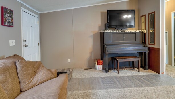 Una sala de estar con un sofá color beige, un televisor sobre un piano y una puerta con un cartel en la pared.