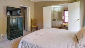 Ein Schlafzimmer mit Bett, Kleiderschrank, Fernseher, Stuhl und einem durch eine offene Tür einsehbaren Badezimmer.