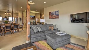 Ein modernes Wohnzimmer mit einer grauen Eckcouch, passendem Hocker und einem Essbereich mit Holzmöbeln.