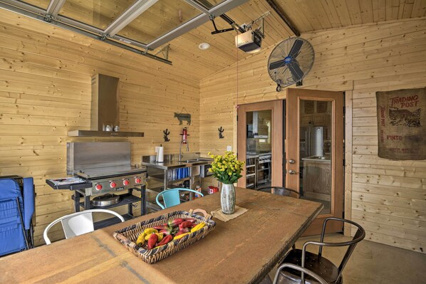 Ein Holzblockhaus-Interieur mit Küchenbereich, einem Esstisch mit Obstkorb, einem Ventilator und einem Kühlschrank.