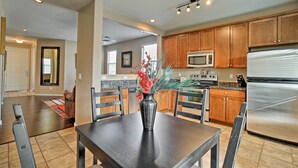 A modern kitchen with wooden cabinets, a stainless steel refrigerator, and a dining area with a table and chairs. - Dog-friendly Arizona Retreat w/ Patio & Grill! (Gilbert)