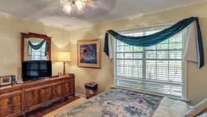 A bedroom with a bed, a dresser, a television, a painting, and a window with curtains.