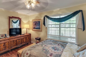 A bedroom with a bed, a dresser, a television, a painting, and a window with curtains.