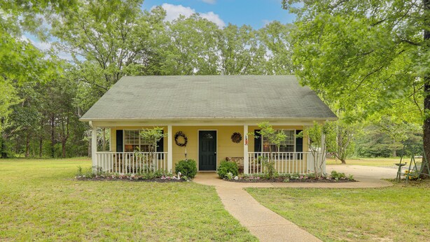A single-story house with a front porch, a front door, and a small garden with flowers and a birdbath.