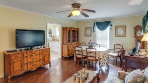 A living room with a television, wooden cabinet, dining table, floral chairs, and a ceiling fan.