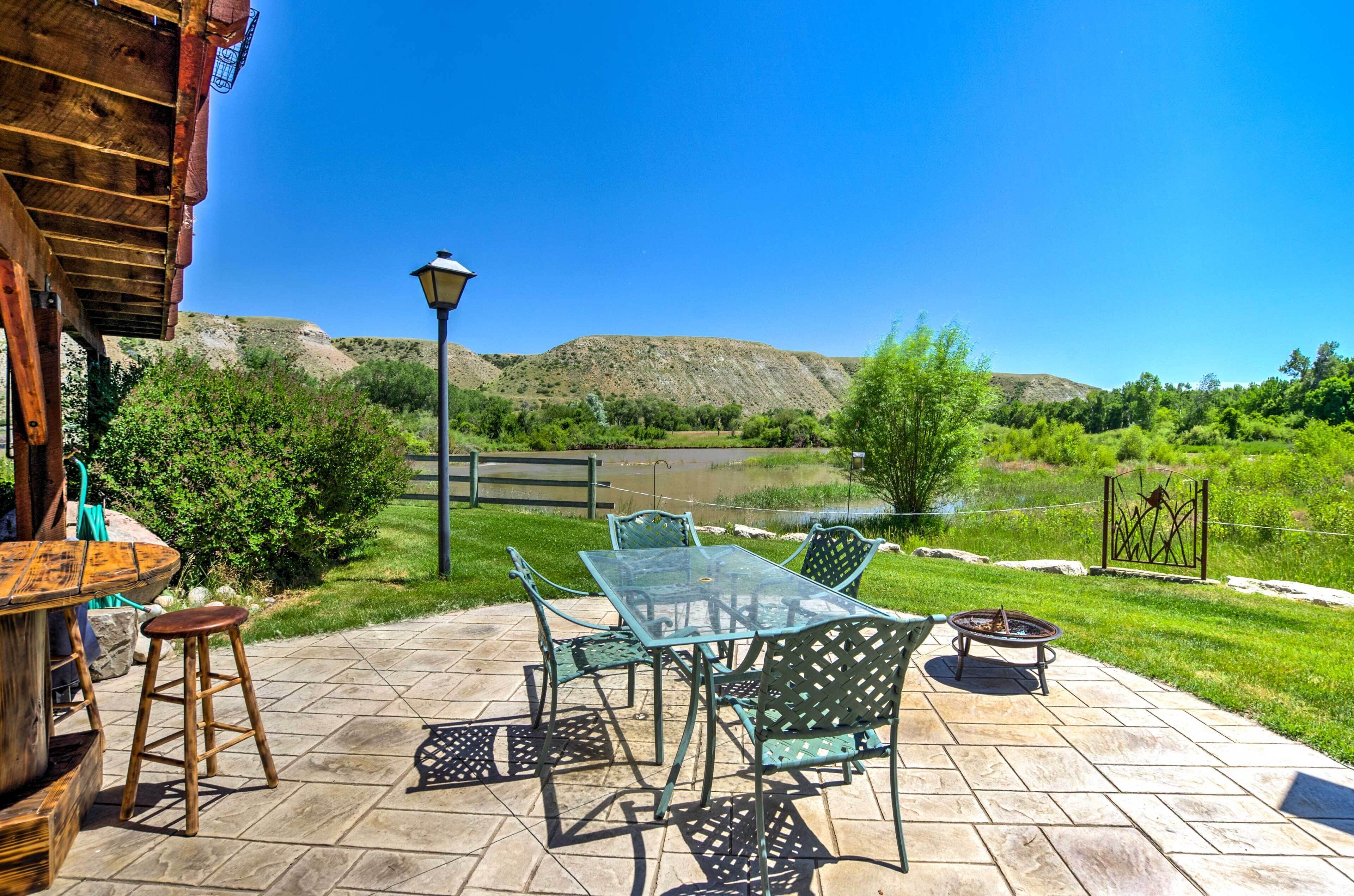 Eine Terrasse im Freien mit Glastisch und -stühlen, einer Feuerstelle und Blick auf eine natürliche Landschaft.