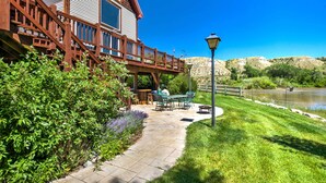 A house with a wooden deck, a patio with outdoor furniture, and a view of a lake. - Stunning Silesia Home: Furnished Deck + River View (Joliet)