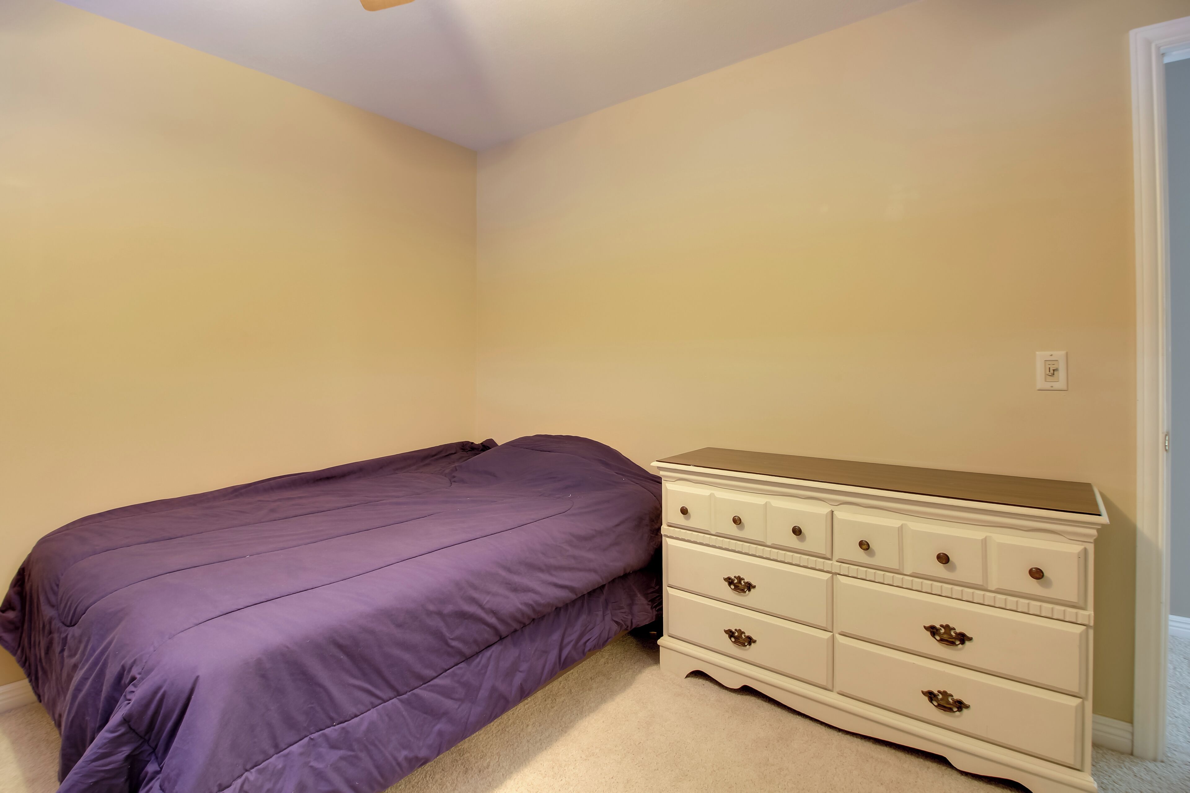 Un dormitorio con cama, cómoda y paredes color beige.