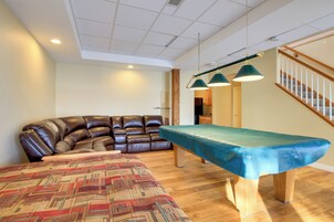 Una sala de estar con mesa de billar, sofá de cuero, alfombra estampada y suelo de madera.