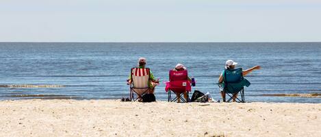 Tres personas sentadas en sillas de playa mirando al océano.