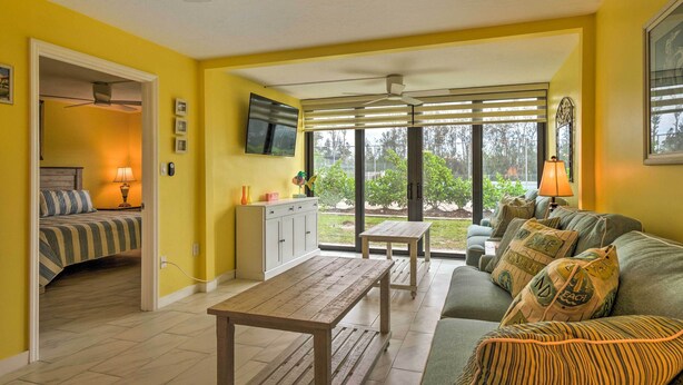 A bright yellow room with a bed, a dining table, and a sofa. There is a TV mounted on the wall and a window with blinds. - Cheery Condo With Pool Access: 3 Miles to Beach! (Fort Myers)