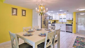 A dining area with a table set for four, surrounded by white chairs, in a room with yellow walls and white cabinets. - Cheery Condo With Pool Access: 3 Miles to Beach! (Fort Myers)