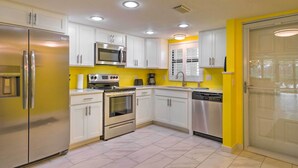 A modern kitchen with white cabinets, stainless steel appliances, and a yellow accent wall. - Cheery Condo With Pool Access: 3 Miles to Beach! (Fort Myers)
