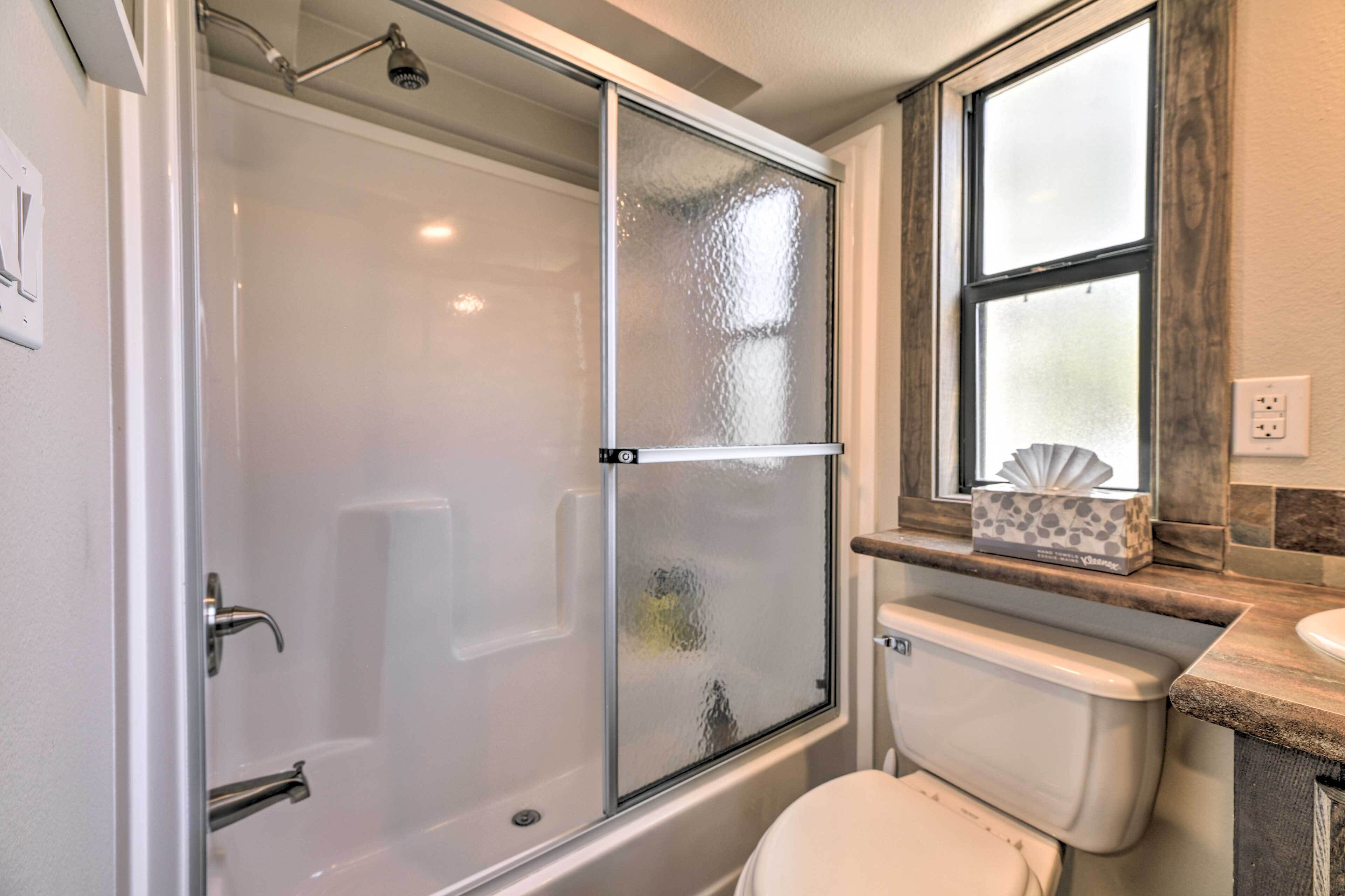 Une salle de bain avec une douche à parois de verre, des toilettes et une fenêtre au-dessus du lavabo.