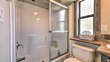 Une salle de bain avec une douche à parois de verre, des toilettes et une fenêtre au-dessus du lavabo.