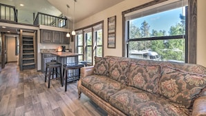 A spacious living area with a large window, a sofa, and a kitchen area with a bar. - Roomy Pagosa Springs Tiny Cabin: 1 Mi to Downtown (Pagosa Springs)
