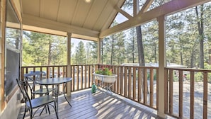 A wooden deck with a table and chairs, a planter with flowers, and a view of a forest. - Roomy Pagosa Springs Tiny Cabin: 1 Mi to Downtown (Pagosa Springs)