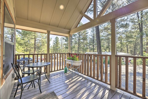 A wooden deck with a table and chairs, a planter with flowers, and a view of a forest. - Roomy Pagosa Springs Tiny Cabin: 1 Mi to Downtown (Pagosa Springs)