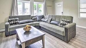 A modern living room with a sectional sofa, a coffee table, and a large window with curtains. - Family-friendly Keansburg Home: Walk to Beach! (Keansburg)