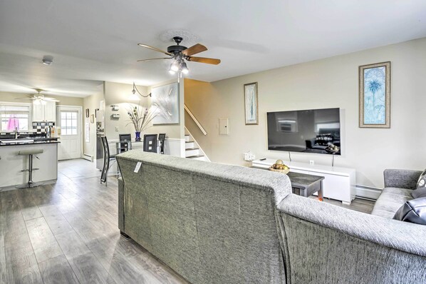 A modern living room with a grey sofa, a flat-screen TV, and a ceiling fan. - Family-friendly Keansburg Home: Walk to Beach! (Keansburg)