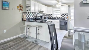 A modern kitchen with white cabinets, a black and white checkered backsplash, a bar area with stools, and a ceiling fan. - Family-friendly Keansburg Home: Walk to Beach! (Keansburg)