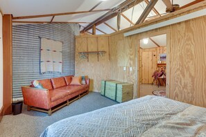 Een kamer met een houten plafond, een rode leren bank, een bed met een decoratief sprei en een groene dressoir.