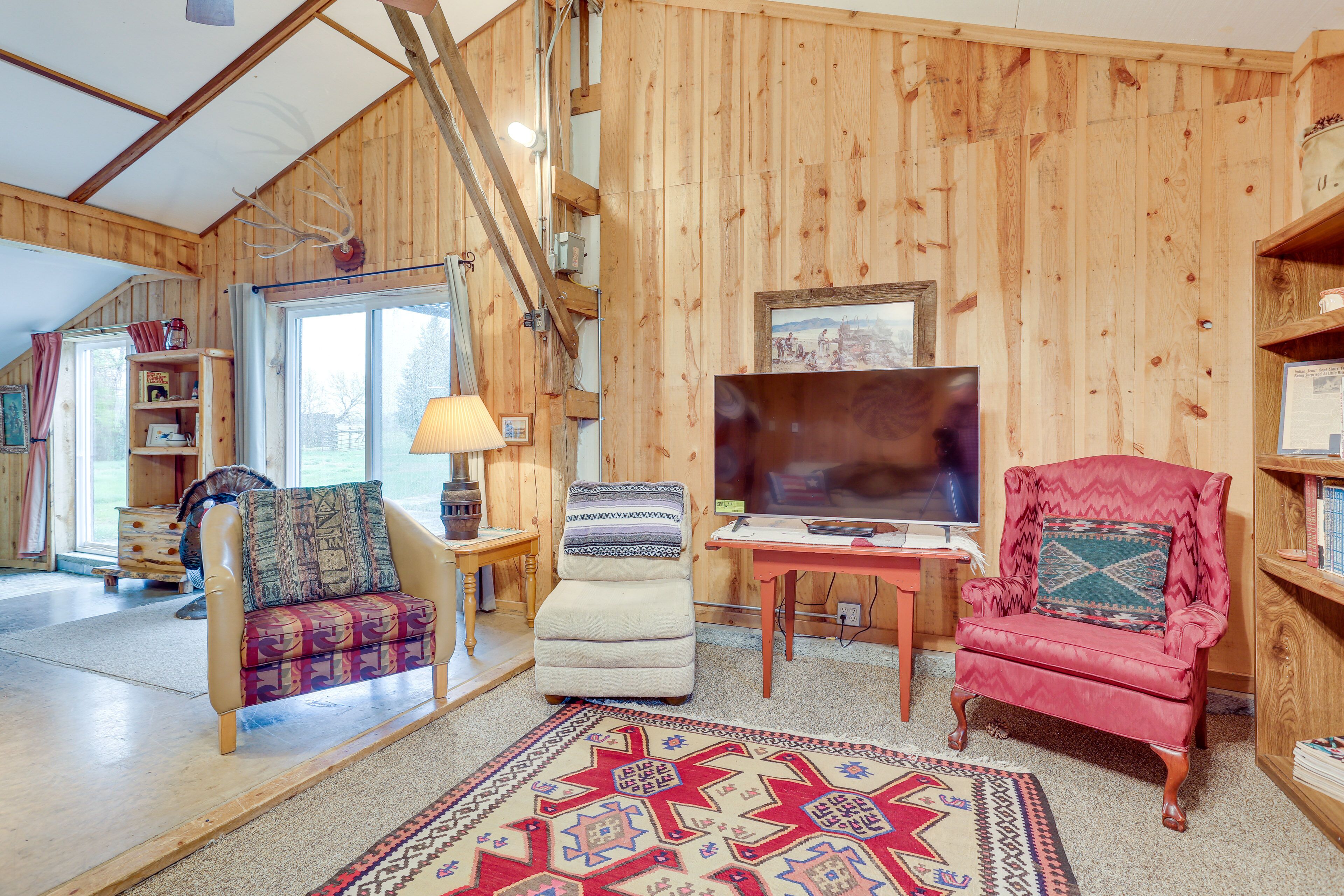 A cozy living room with wooden walls, a large TV, and two armchairs.