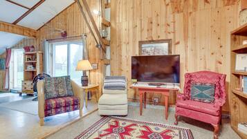 A cozy living room with wooden walls, a large TV, and two armchairs.