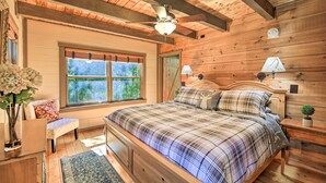 A wooden cabin bedroom with a bed, a bench, a window, and a ceiling fan. - 9 Mi to Sugar Mountain: Stunning Cabin w/ Views (Banner Elk)