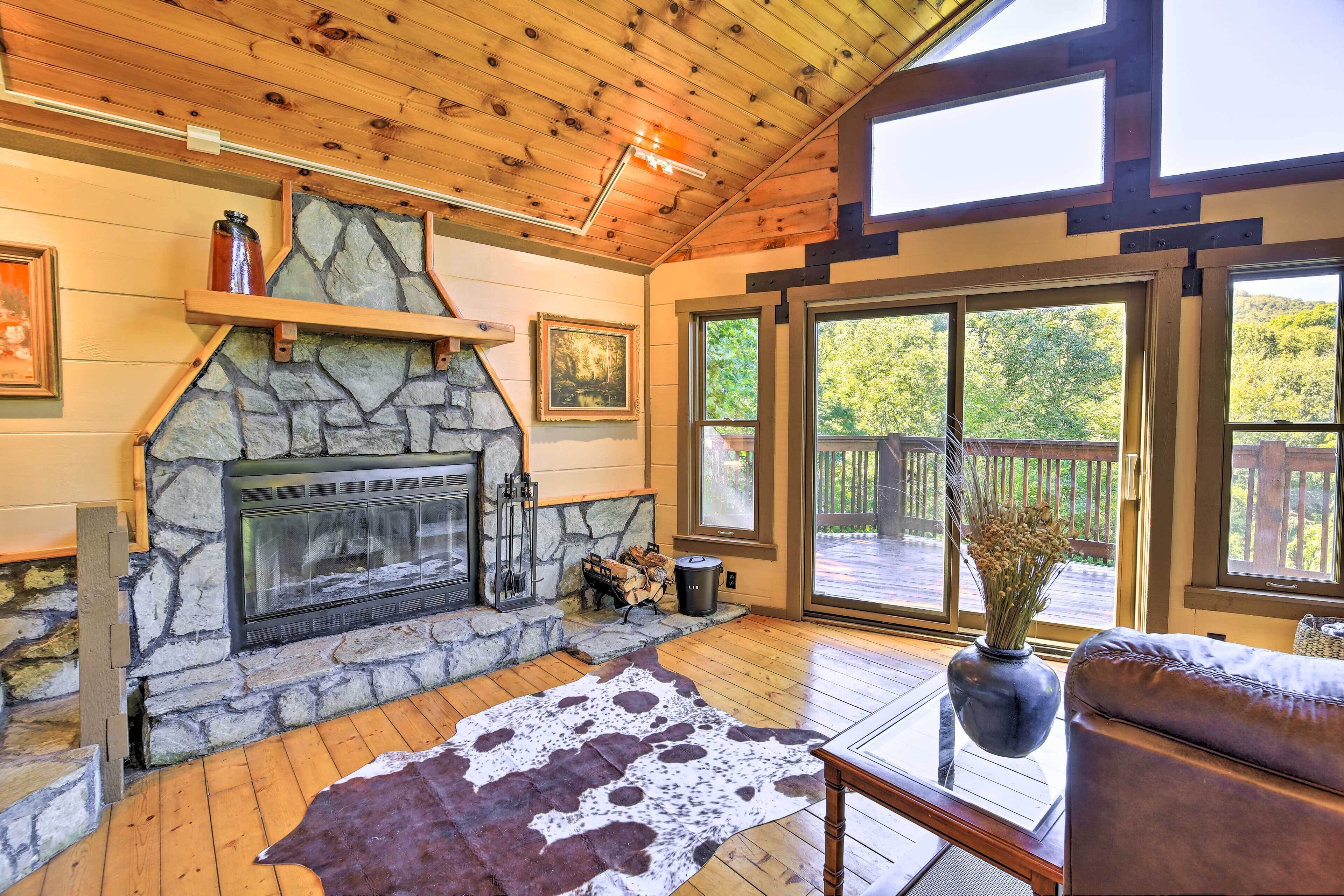 Una habitación acogedora con chimenea de piedra, suelo de madera y ventanas amplias con vistas al exterior.