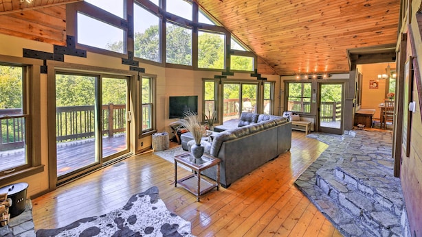 A spacious living area with a large gray sofa, a coffee table, and a stone accent wall. - 9 Mi to Sugar Mountain: Stunning Cabin w/ Views (Banner Elk)