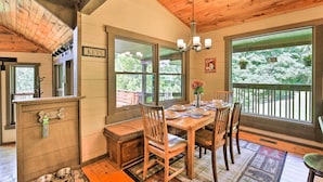 A wooden dining area with a bench, a table set for four, and large windows offering views of greenery. - 9 Mi to Sugar Mountain: Stunning Cabin w/ Views (Banner Elk)