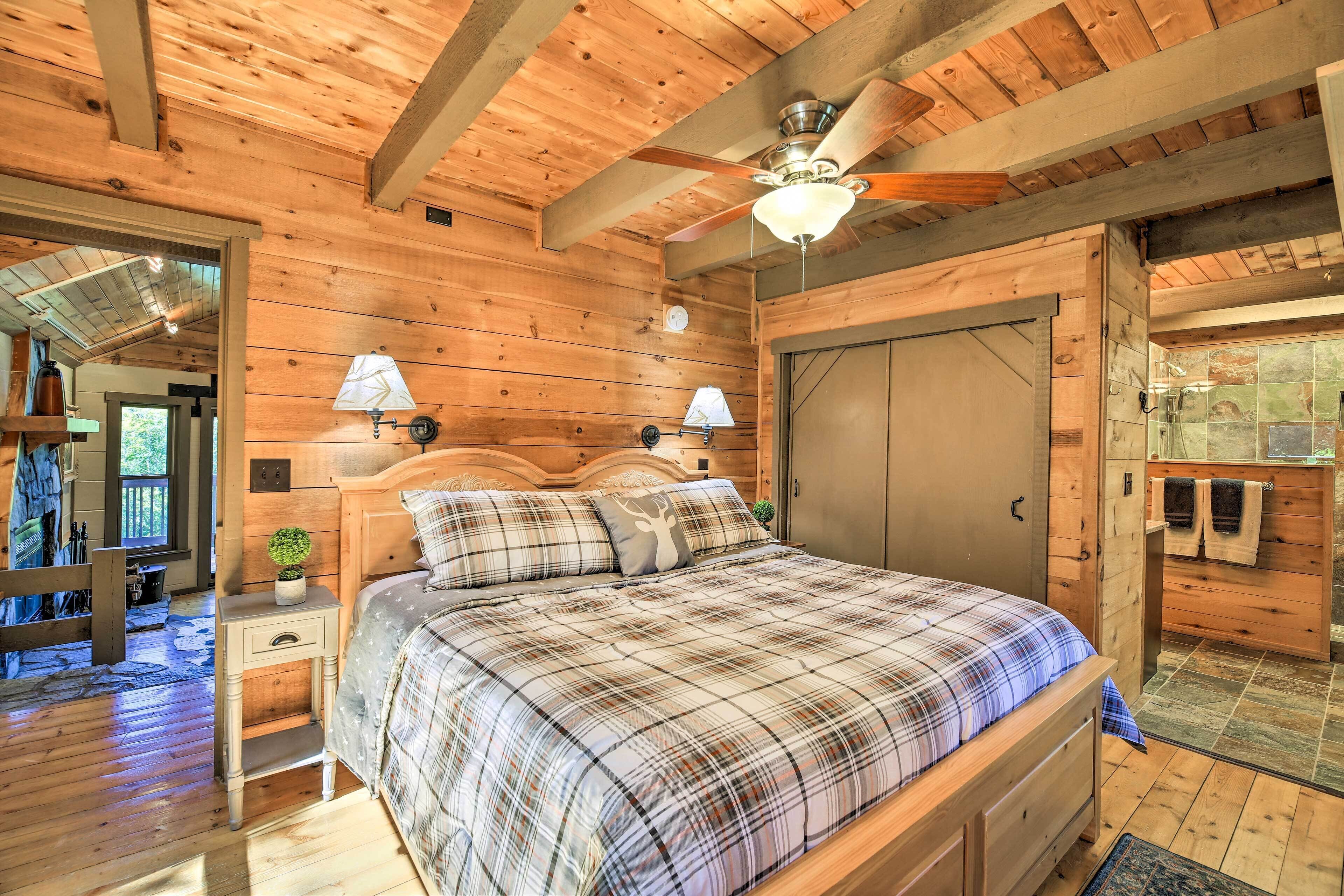 A wooden cabin bedroom with a bed, two bedside lamps, a ceiling fan, and a door leading to a bathroom.