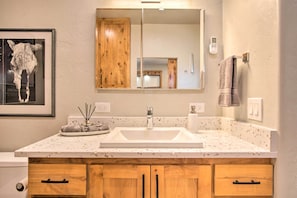 A bathroom with a white sink, wooden cabinets, a framed picture on the wall, and a towel hanging on a towel rack. - Tucson Studio ~ 10 Mi to Downtown & U of A (Tucson)