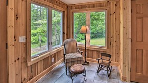 A wooden-paneled room with large windows, a striped armchair, a rocking chair, and a floor lamp. - Rustic Sunset Escape on 67 Acres: Outdoor Kitchen (Sunset)