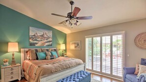 A bedroom with a bed, a nightstand, a bench, a ceiling fan, and a large window with blinds. - AZ Home w/ Resort-style Amenities & Mtn View! (Saddlebrooke)